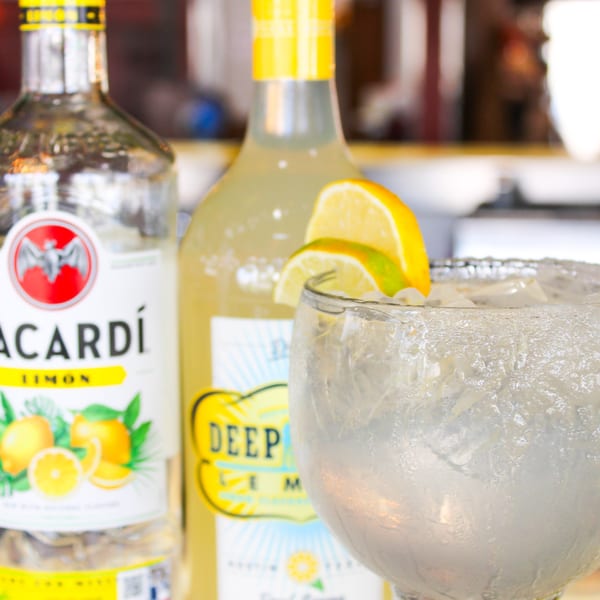 A margarita with lime and lemon slices, next to bottles of Bacardi Limon and Deep Eddy Lemon.
