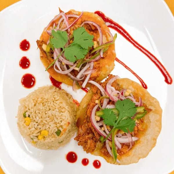 Two Mexican sopes topped with shredded meat, red onions, and cilantro, served with rice and red sauce.