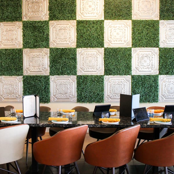 A long dining table set with orange napkins and glasses, against a green and white checkered wall.