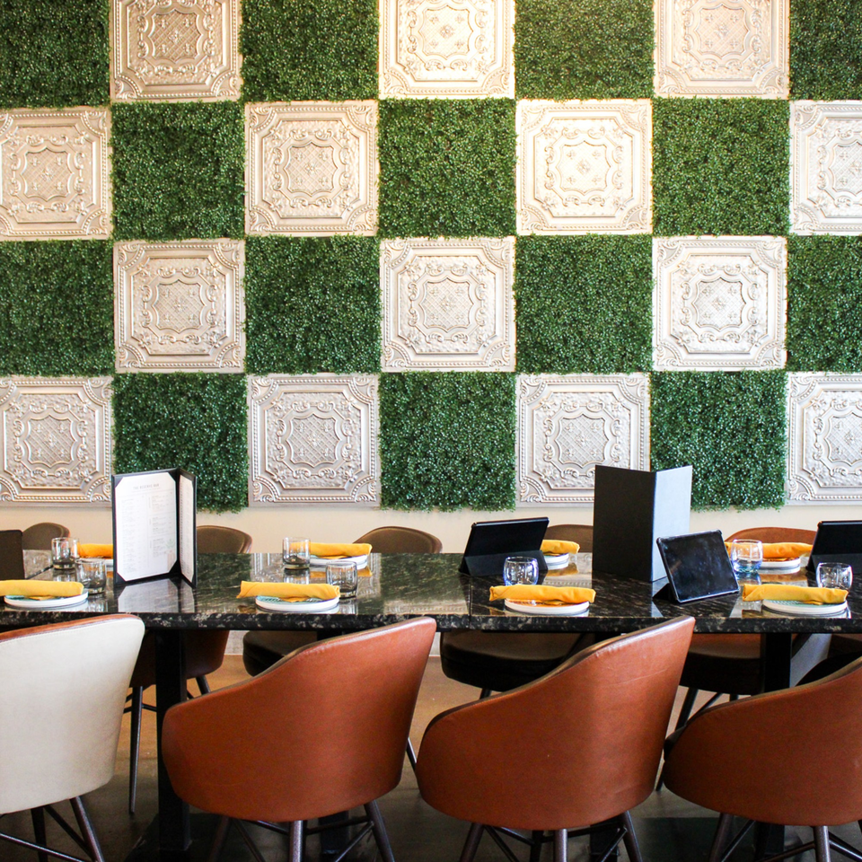 A long dining table set with orange napkins and glasses, against a green and white checkered wall.