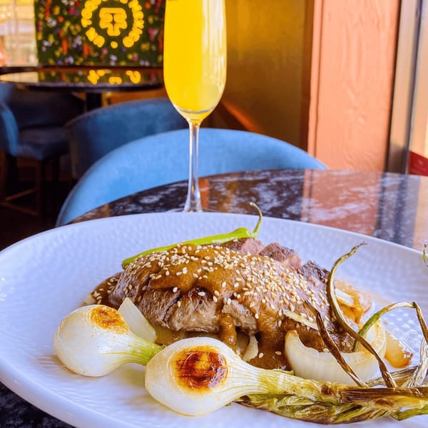 Mexican dish with meat, mole sauce, sesame seeds, grilled onions, and a mimosa.