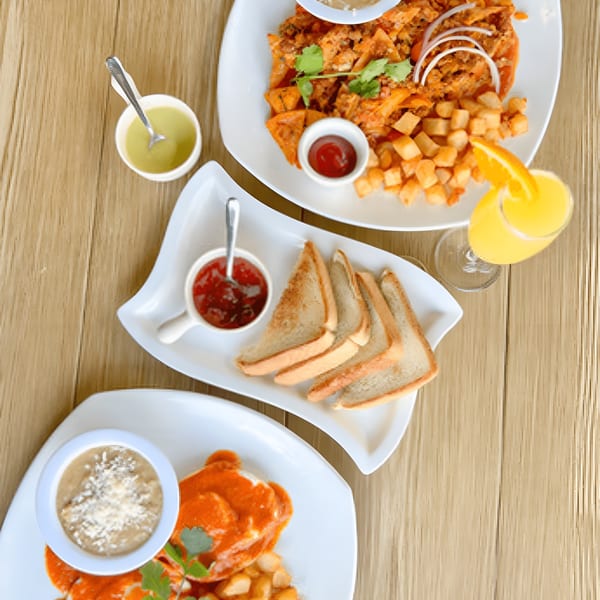 Overhead view of three plates of Mexican breakfast food, including chilaquiles, toast, and orange juice.
