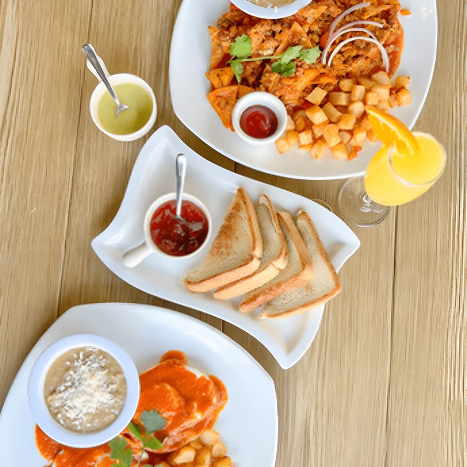 Overhead view of three plates of Mexican breakfast food, including chilaquiles, toast, and orange juice.