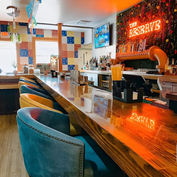 The Reserve bar with colorful stools, a neon sign, and a vibrant, eclectic decor.