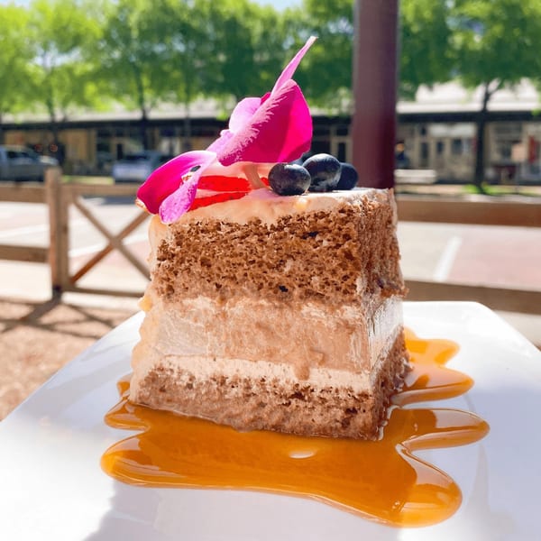 A slice of layered cake with berries and a pink orchid, drizzled with caramel sauce, outdoors.