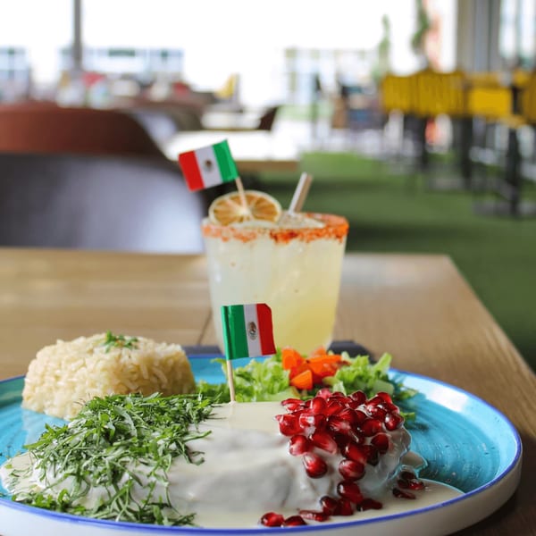 Mexican dish with white sauce, pomegranate, and herbs, served with rice and a margarita.