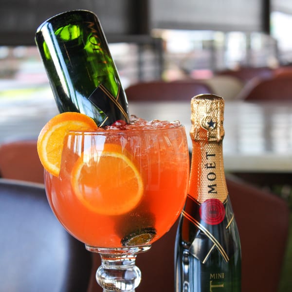 A large orange cocktail with orange slices and a mini Moët champagne bottle inverted into it.
