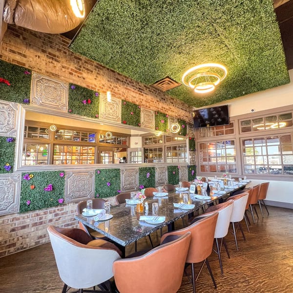 A long dining table set for guests in The Reserve, with a green wall and brick accents.