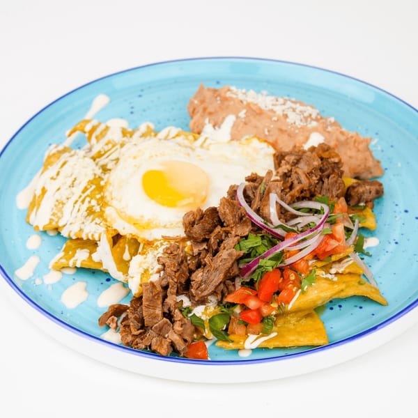 Mexican chilaquiles with shredded beef, a fried egg, refried beans, and fresh salsa on a blue plate.