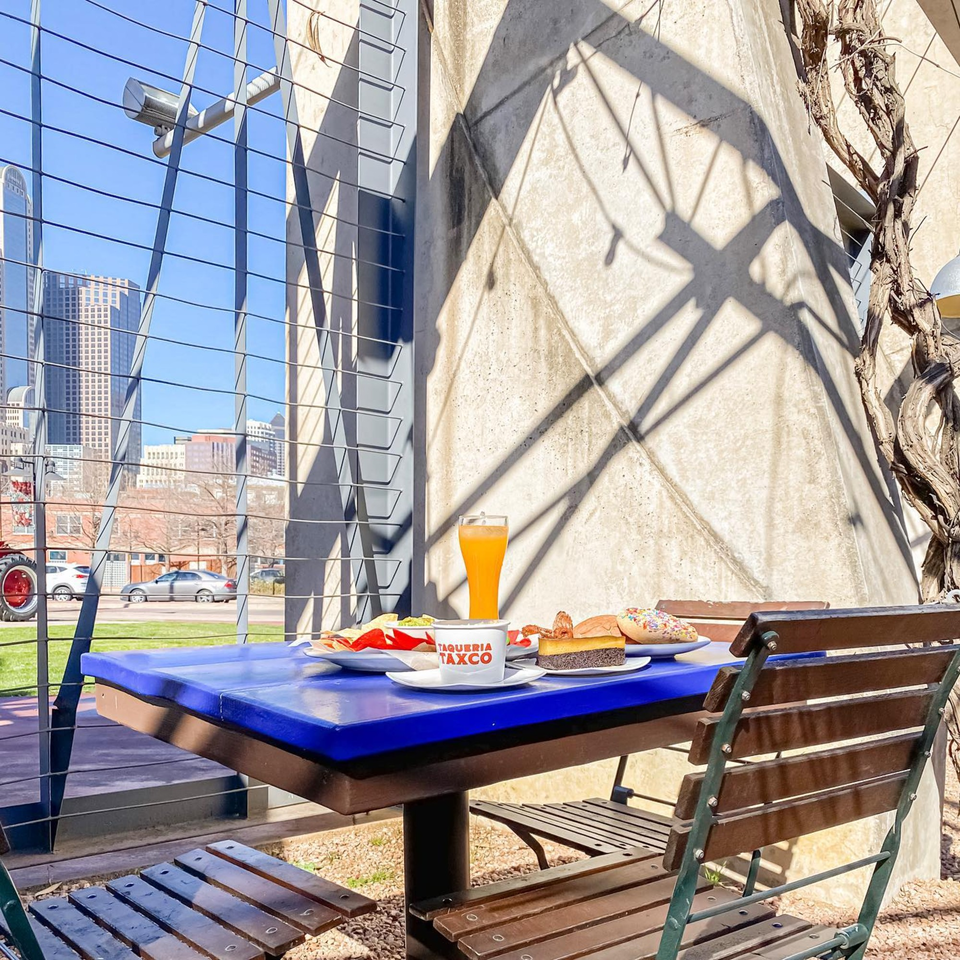 A blue outdoor table at The Reserve with Mexican food, drinks, and city buildings in the background.