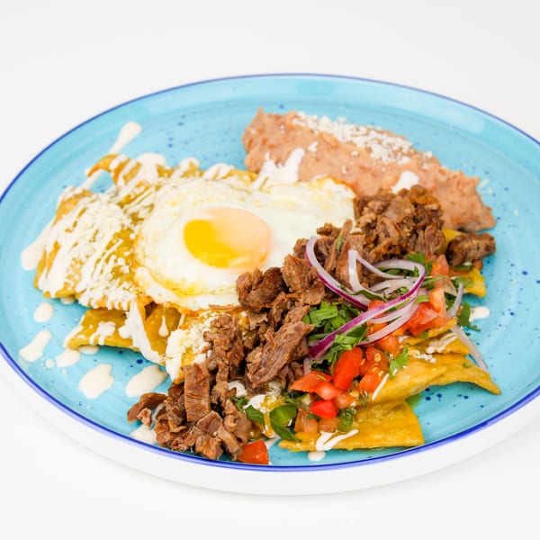 Chilaquiles with steak, a fried egg, refried beans, and pico de gallo on a blue plate.