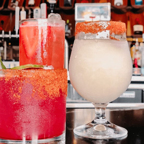 Three vibrant Mexican cocktails on a bar, two red and one frozen white, all with spiced rims.