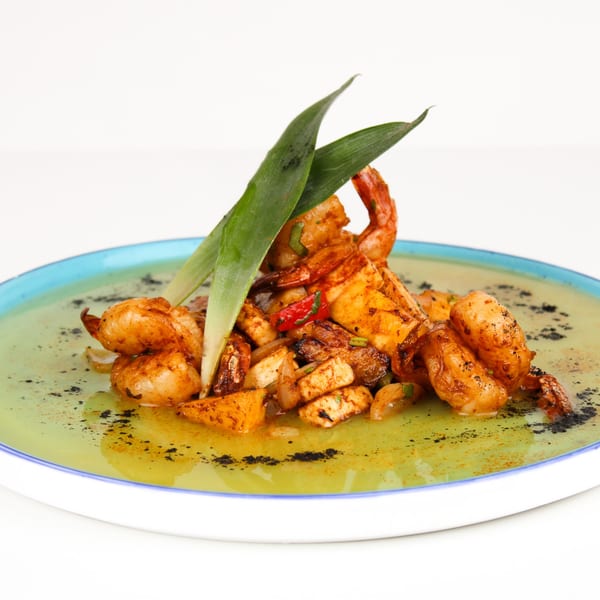 Mexican shrimp and squid dish with red peppers, onions, and green garnish on a blue-rimmed plate.